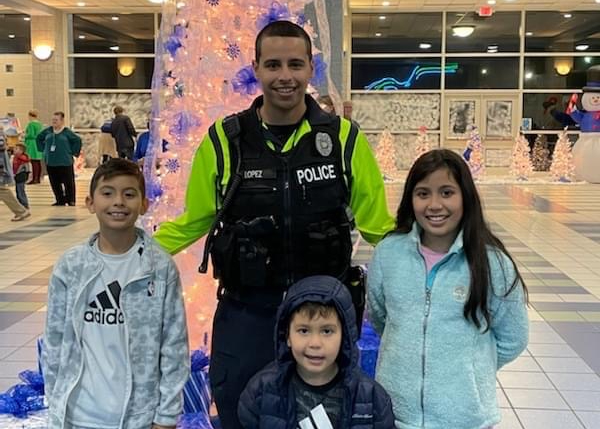 School Resource Officer Lopez with JV students in front of a white Christmas tree